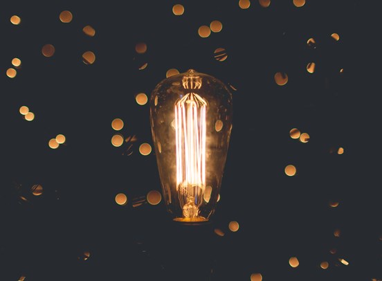 A warm yellow lightbulb surrounded by glittering flecks of gold.