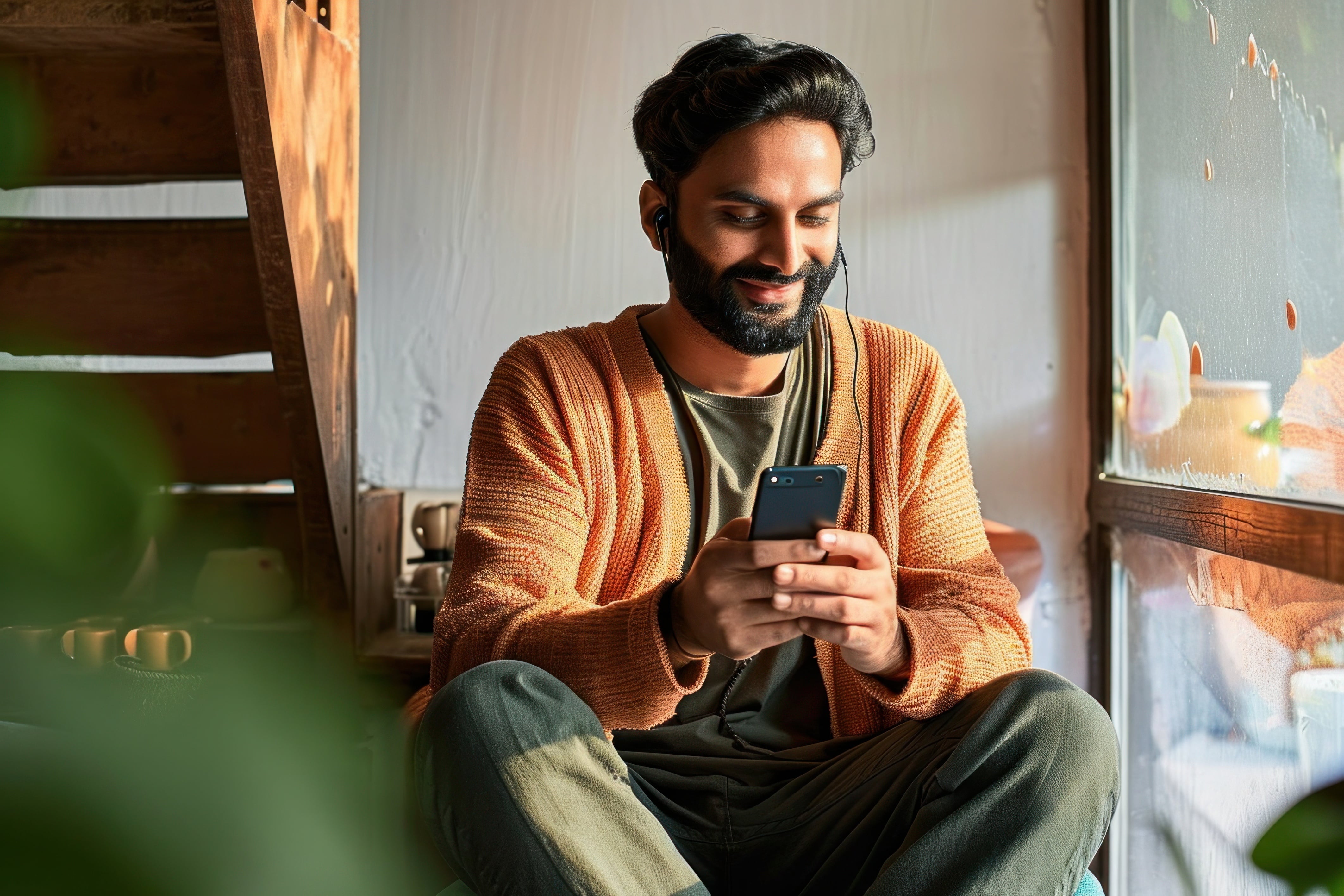 Man wearing an orange cardigan scrolling on a smartphone.