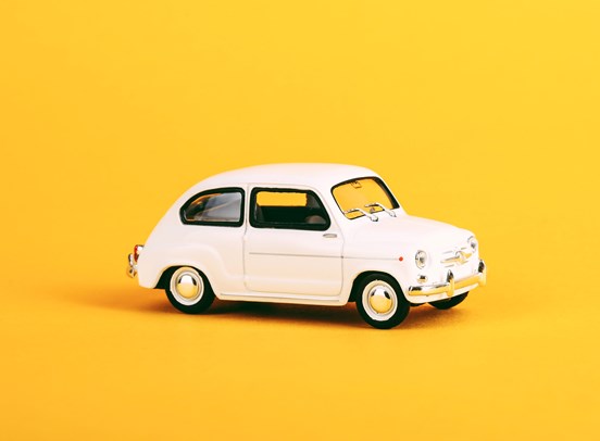 A white toy car, with a yellow background.