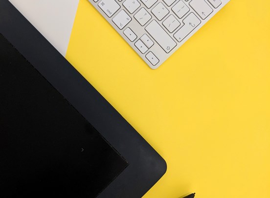 A desktop monitor and keyboar parallel to one another at a 45 degree angle on a light yellow background.