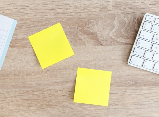 A wood grain office desk, with two blank sticky notes stuck on it.