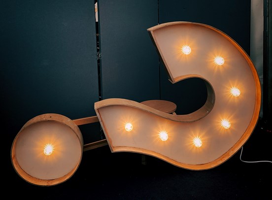 A large question mark (?) sign with lit up lightbulbs inside of it.