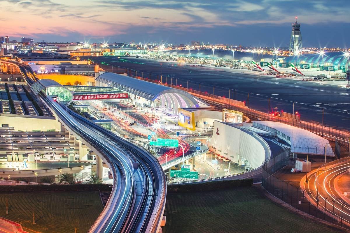 Dubai International Airport at dusk, with the metro, terminal and Emirates aircraft