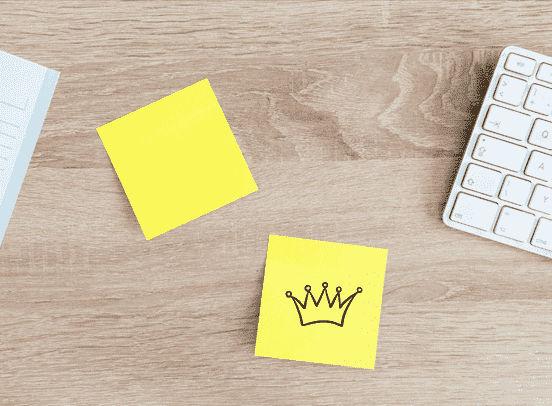 Two yellow post it notes on an office table, the left one blank, and the right one with a crown drawn on it.