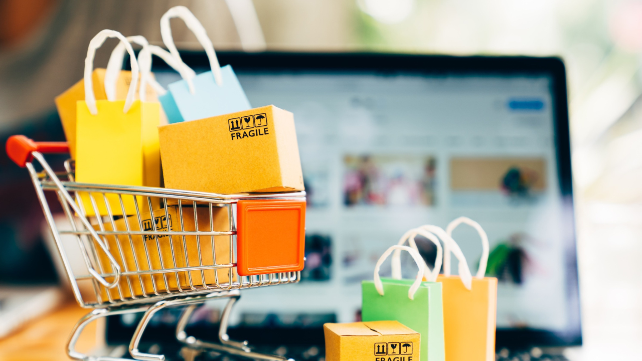 A toy shopping cart filled with mini shopping bags and boxes, on an open laptop