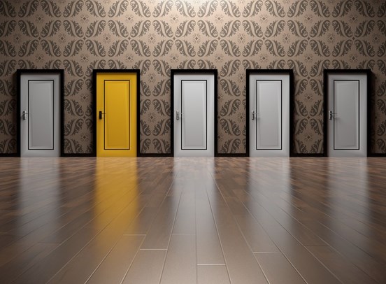 A yellow door amongst 4 other white doors. The yellow door is second from the left. The flooring is wooden, with a 50's inspired pattern wallpaper decorating the walls.