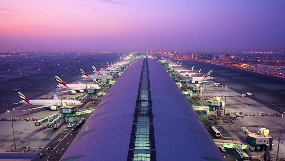 Emirates aircraft parked along the Dubai International terminal at dusk.