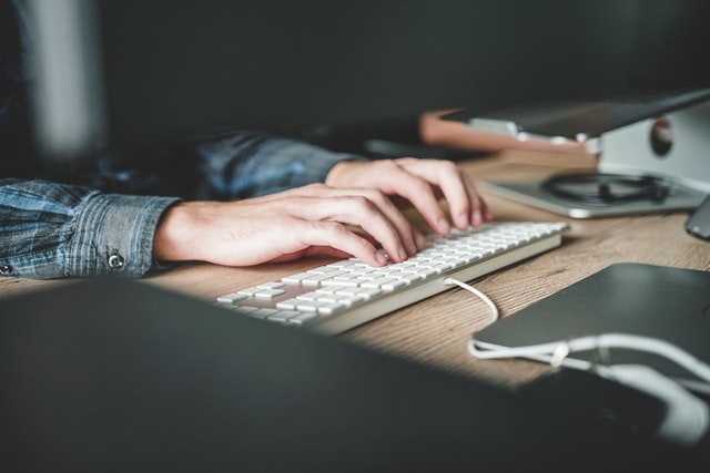 A persons hands tapping away at a white keyboard, with a monitor above