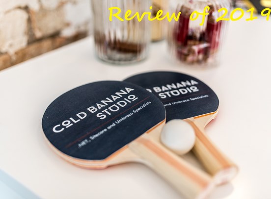 2 table tennis rackets featuring the print "Cold Banana Studio - .NET, Sitecore and Umbraco Specialists", with a ping bong ball wedged between them. In the top right hand corner is the text "Review of 2019" superimposed.